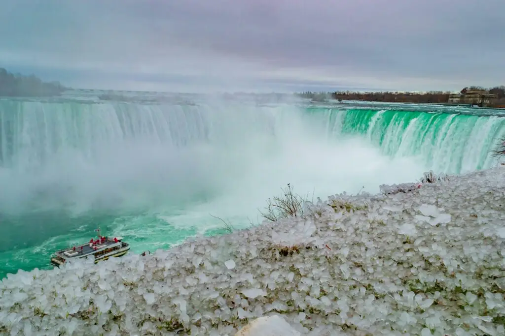 Voyage sur mesure en Amériques – Vue des chutes du Niagara au Canada, partiellement gelées en hiver avec un bateau touristique en contrebas.