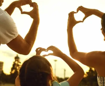 Parents et enfant formant des cœurs avec les mains, geste symbolique d’un voyage en famille réussi.