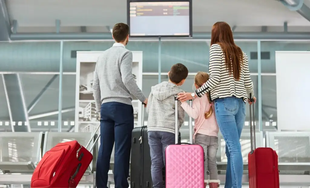 Famille avec enfants regardant les écrans d’affichage des vols à l’aéroport, valises prêtes pour le départ. -voyager en famille