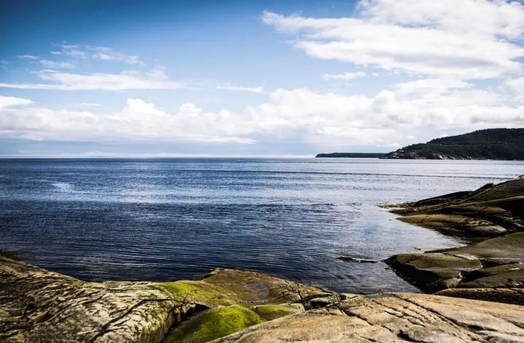 Panorama du fjord du Saguenay au Canada avec rochers en premier plan et collines boisées à l’horizon sous un ciel nuageux - que faire au Canada